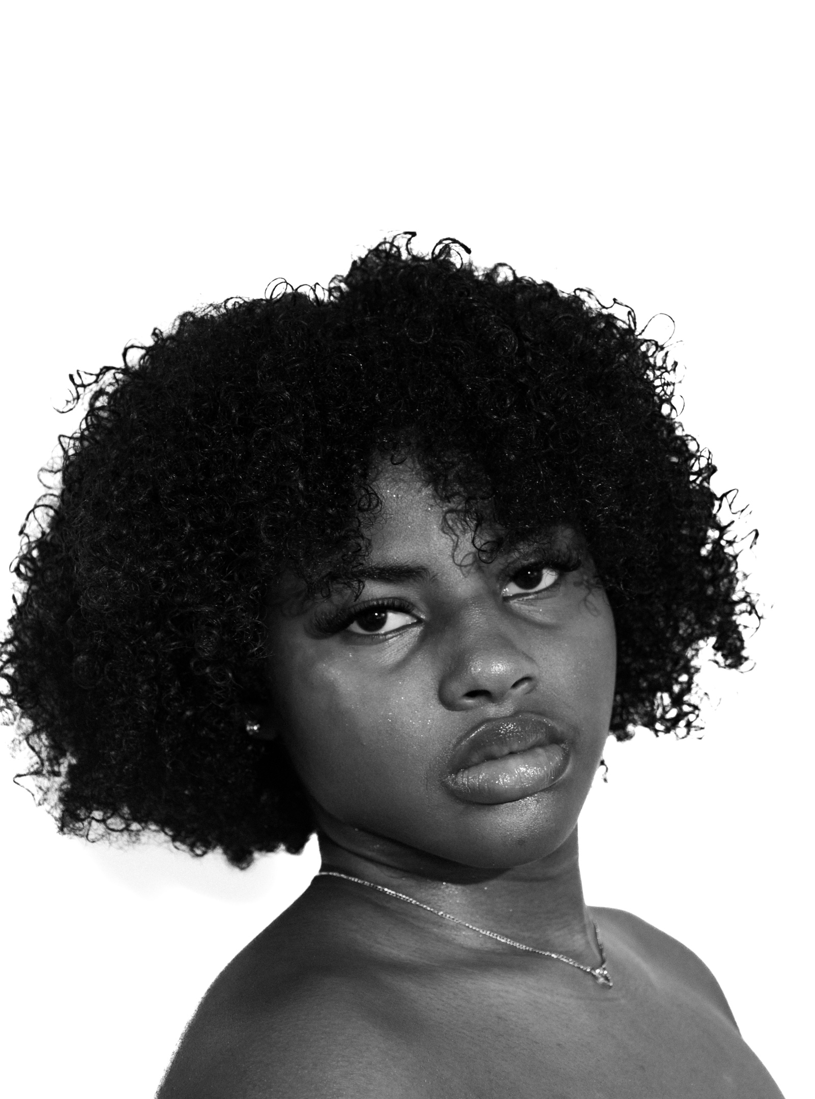 Headshot of Kenyla Jackson, a smiling young black woman with her dark hair pulled high on top of her head. She has a small nose piercing stud and is wearing an off-shoulder pink sweater