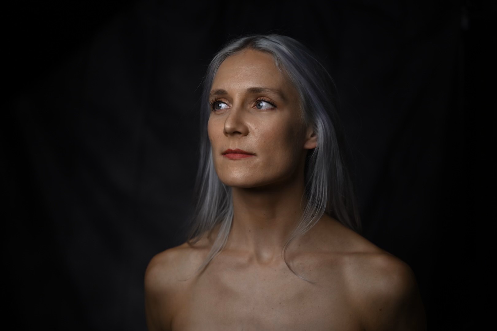 Headshot of Stephanie - A white woman with silver/purple hair, blue eyes, and a lean, athletic build against a black background