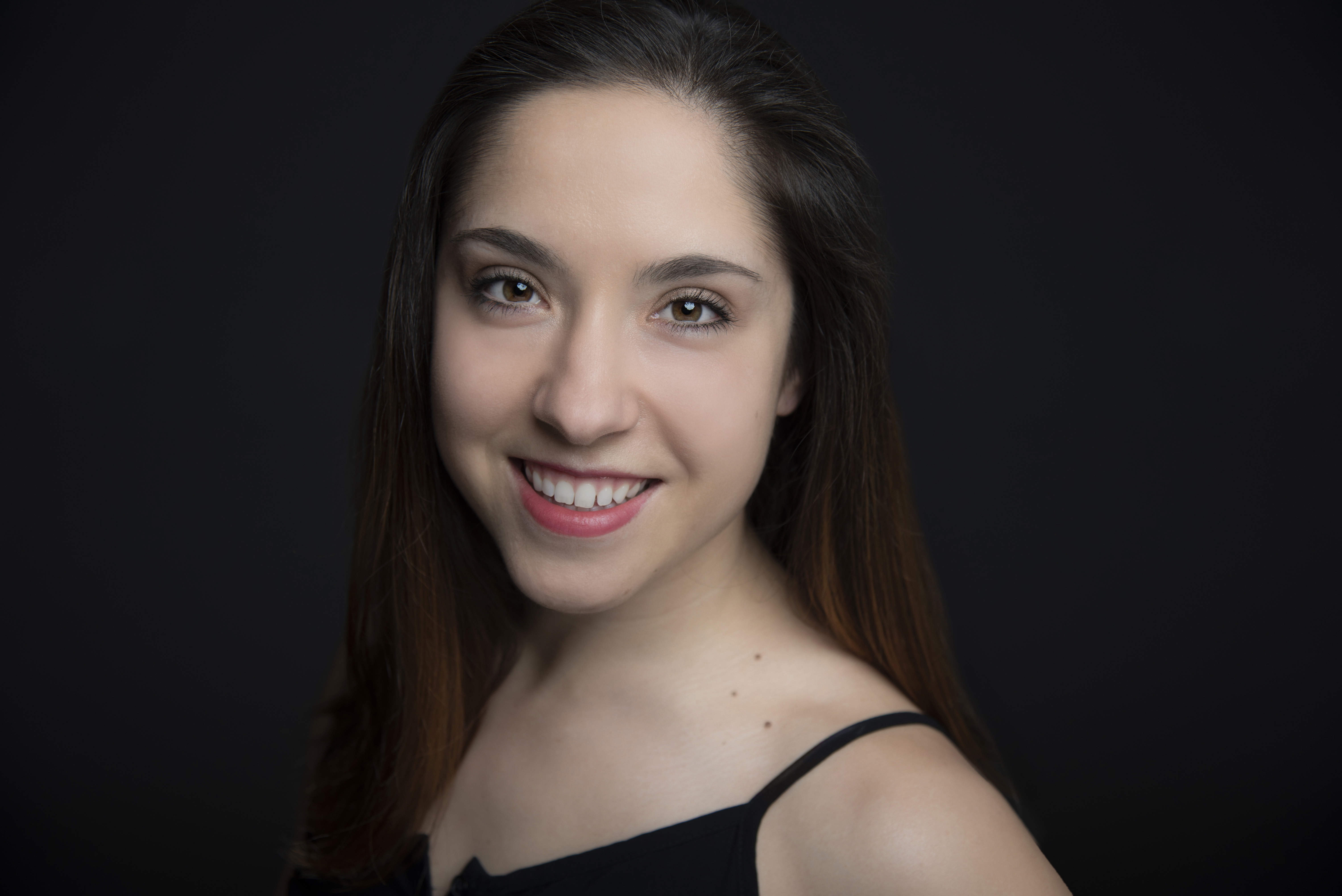 Headshot of Katy - a smiling white woman with brown hair and brown eyes against a black background